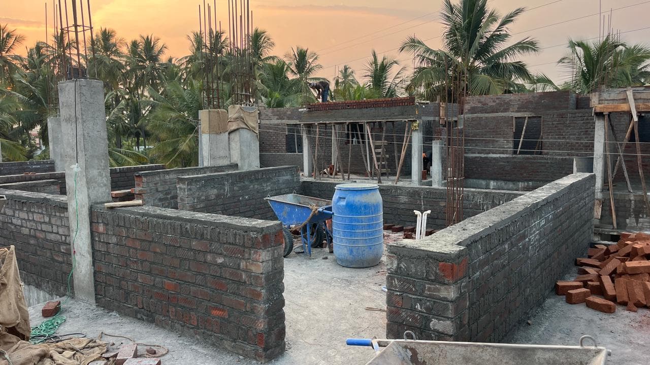 Ground-floor brick walls rising between concrete columns, with a wheelbarrow and stacked bricks