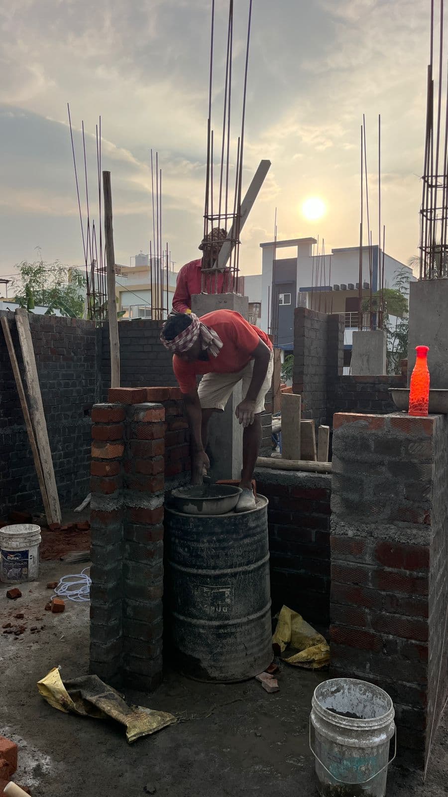 Masons laying brickwork beside reinforcement bars, the sun low behind